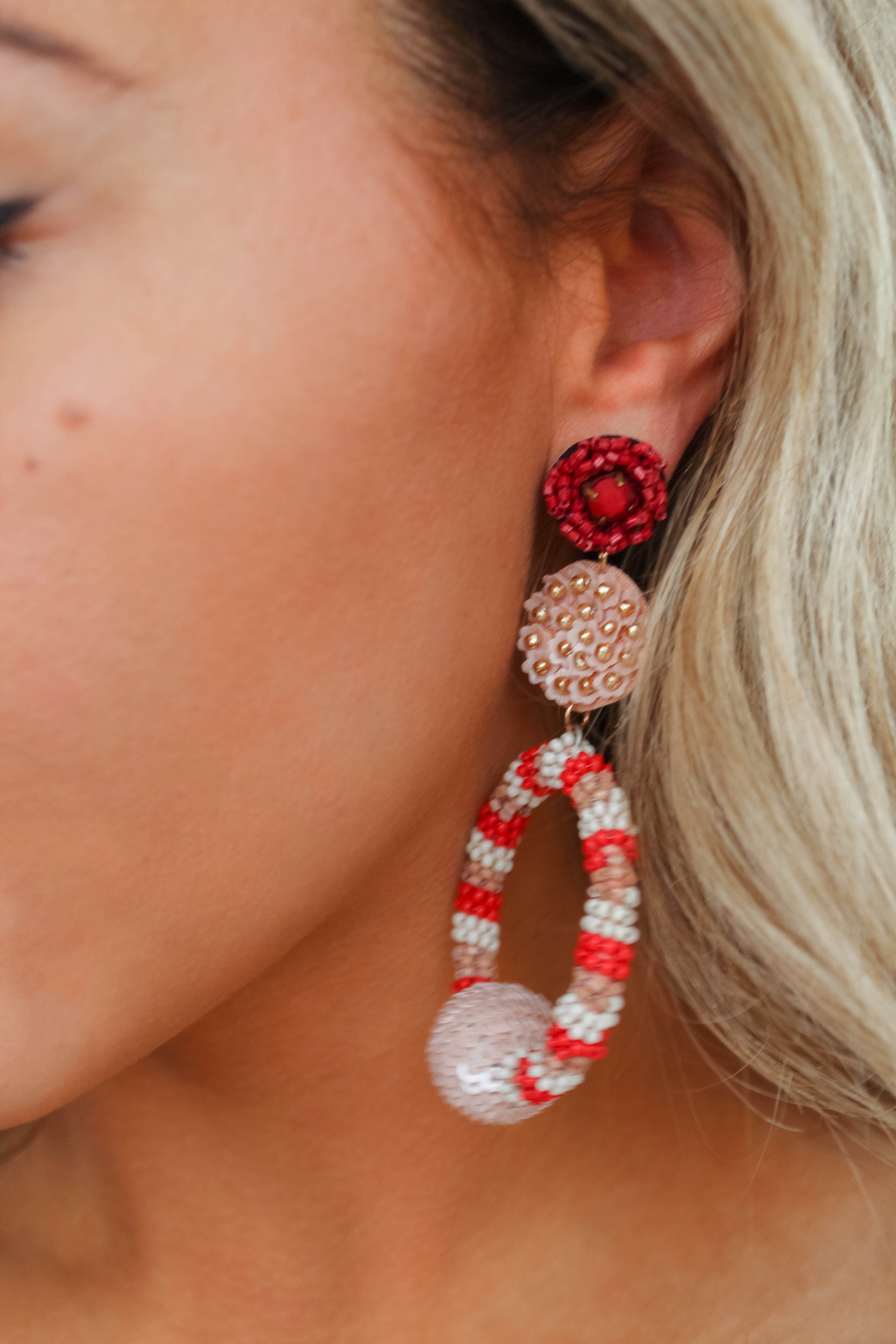 A close-up image of a woman wearing beaded dangle earrings with a floral design in red, pink, and white colors.
